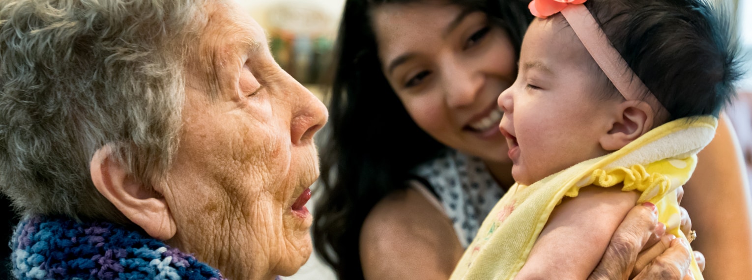 vacunas-header.jpg Abuela con su nieta alzando la biznieta y sonriendo.