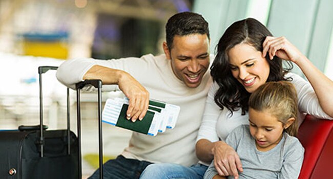vacunas-viaje-650px.jpg Padre, madre e hijo mirando un pasaporte sentados en el aeropuerto.