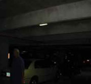 Área de estacionamiento muy oscura con un vehículo y una persona que apenas se ven