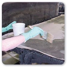 Vista de dos manos con guantes de goma pintando con una brocha una superficie plana