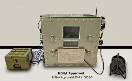 Esta es una foto del aprobado sistema de comunicación magnética MagneLink® de Lockheed Martin. Las palabras "Aprobado por MSHA" y el número de aprobación (23-A110002-0) se muestran debajo de la foto. La caja principal del medio contiene el control de la computadora y baterías de reserva. Un carrete con cables de transmisión se observa a la derecha. La caja pequeña a la izquierda contiene la antena receptora y otros dispositivos eléctricos de recepción.
