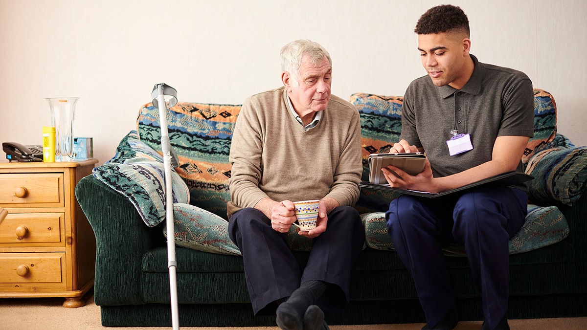 Support worker with client Young man and older man on a couch looking at a clipboard
