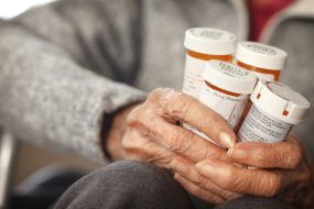 Older adult woman holding several prescription medicine bottles