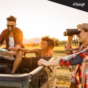 steer-to-your-health Image displays a man reading a map while sitting in the back of a pick-up truck, with a woman ostensibly pointing toward their destination, and another man looking in that direction through a pair of binoculars.