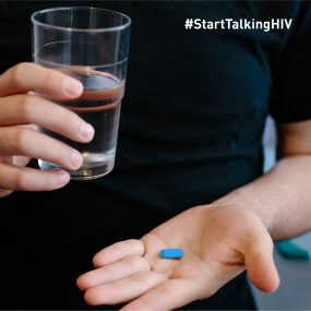 water-and-pill Image displays the upper body of a man who is holding a glass of water in one hand and a blue pill in the palm of his other hand.