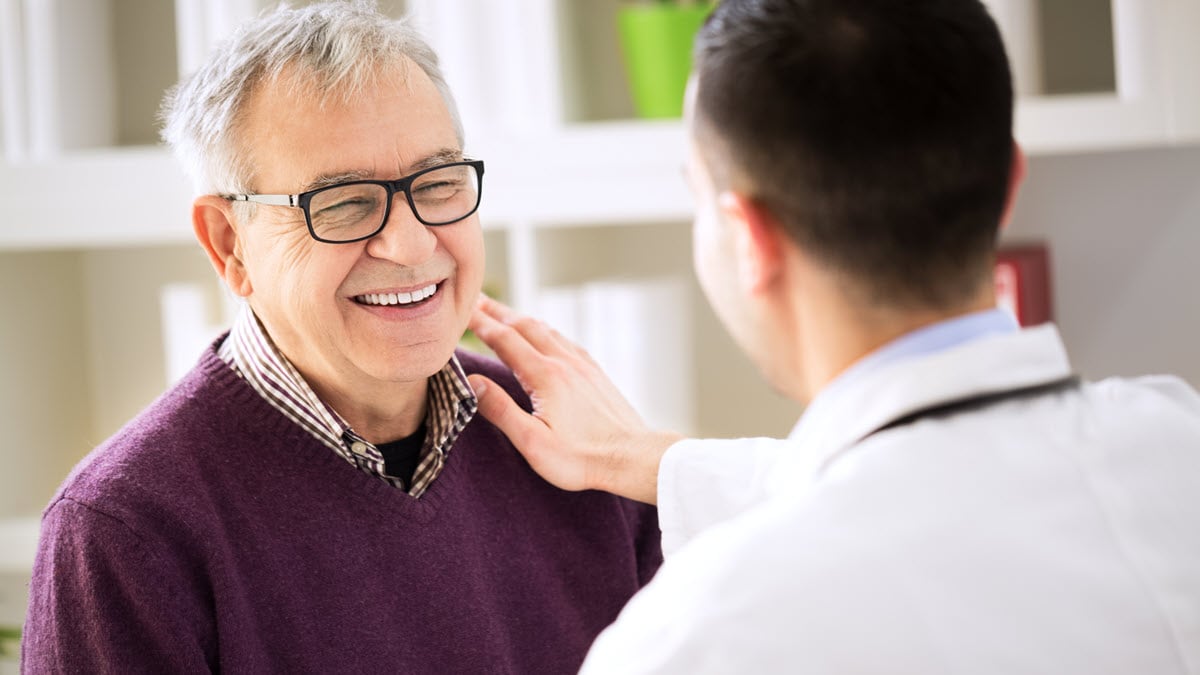 — title missing — A male patient wearing glasses smiles while speaking with a health care provider