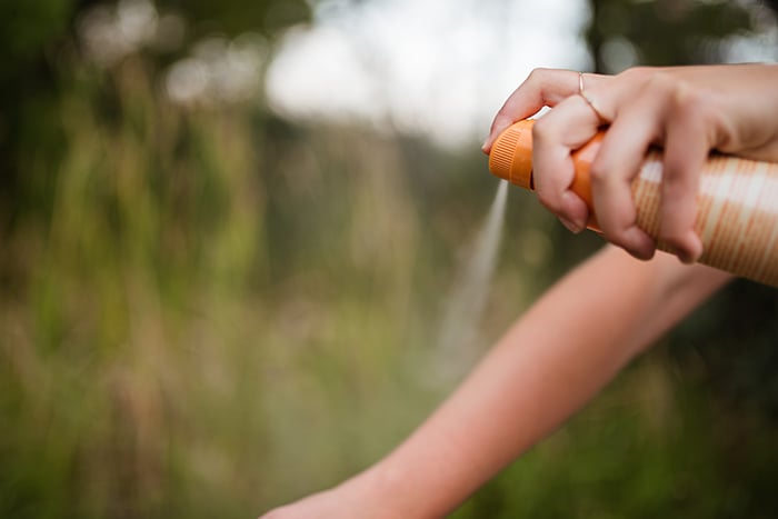 Person spraying insect repellent on their arm.