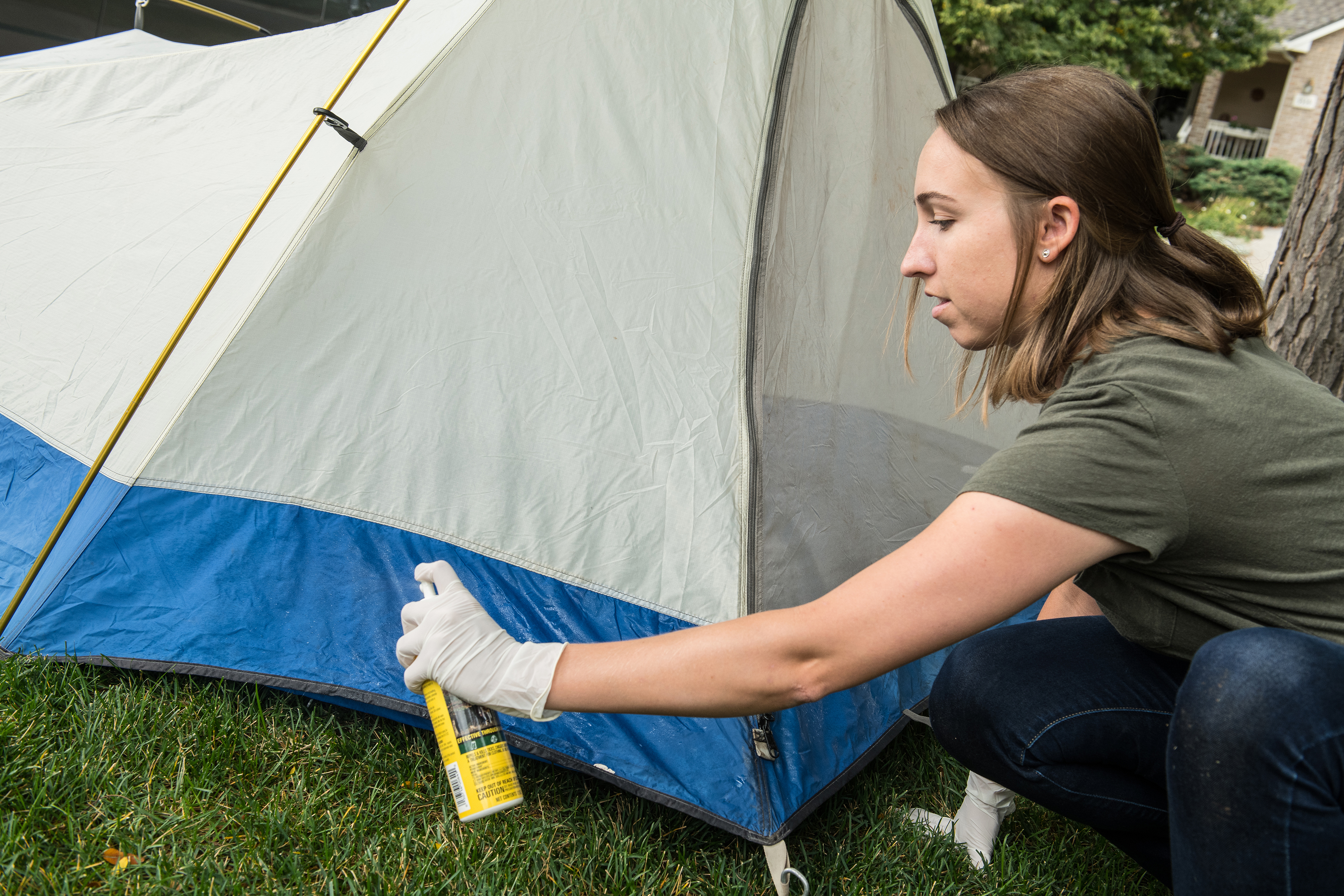 Photo of a woman applying permethrin to the outside of her tent.