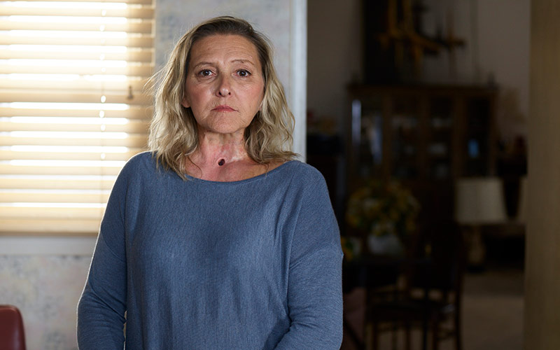 Sharon, a Tips Campaign Participant, is standing in her bedroom, Her stoma shows above a blue blouse.