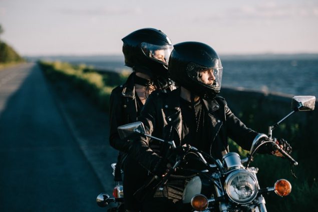 A couple on a motorcycle wearing helmets and jackets