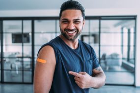 Reasons vaccinate 3 A young man smiling and pointing to his arm after getting his shot.