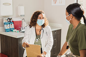 Doctor and female patient sit together wearing masks
