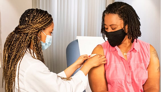 A doctor puts a band aid on a woman after administering a vaccine.