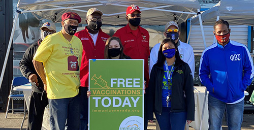 Group of volunteers stand in front of sign: Free Vaccinations Today