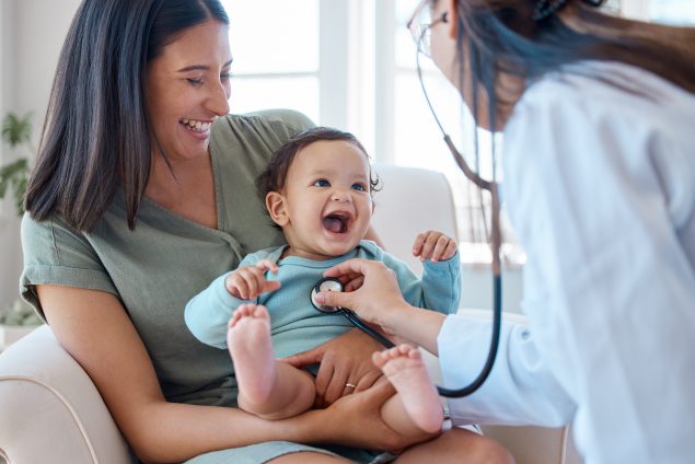 Picture of a baby sitting on her mother's lap while being examined by a doctor