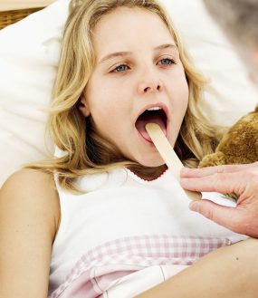 girl-tongue-depressor.jpg Close-up of a doctor putting a tongue depressor into the mouth of a girl.