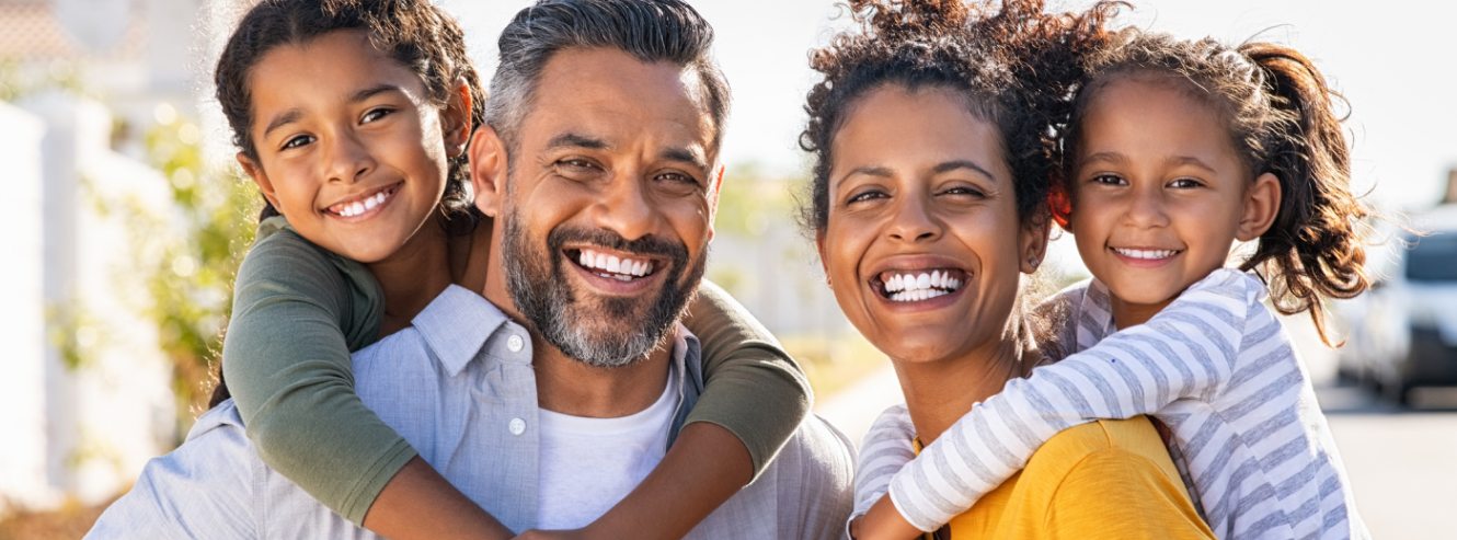 Family of four smiling, with parents holding their kids on their backs