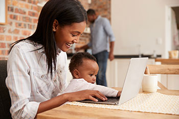 visit-mom-laptop Mom looks up vaccine information on a laptop while holding her baby.