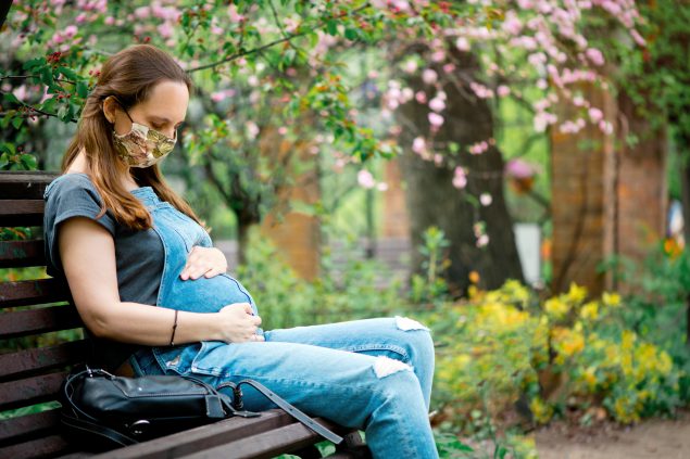 Pregnant woman wearing protective face mask in blooming park Pregnant woman wearing protective face mask in blooming park