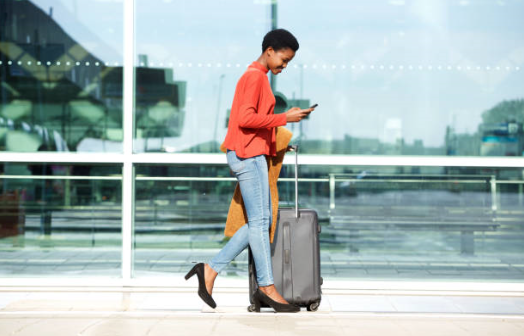 A woman with a suitcase walking through an airport checking her smart phone