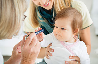 pediatrician-baby-eye-test A mother holding her cute baby girl while the pediatrician does an eyesight test with light pen.