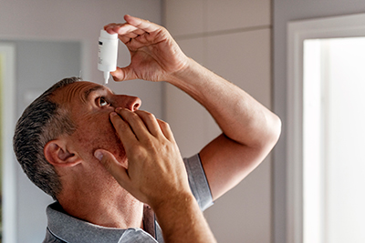 man putting eye drops in eye