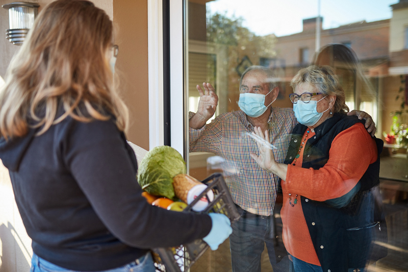 iStock-1220783999 woman looking through window at two elderly people wearing face coverings