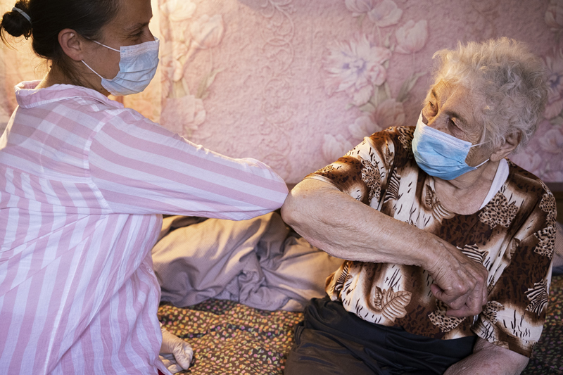 iStock-1254376793 woman wearing face covering elbow bumping with elderly woman wearing face covering