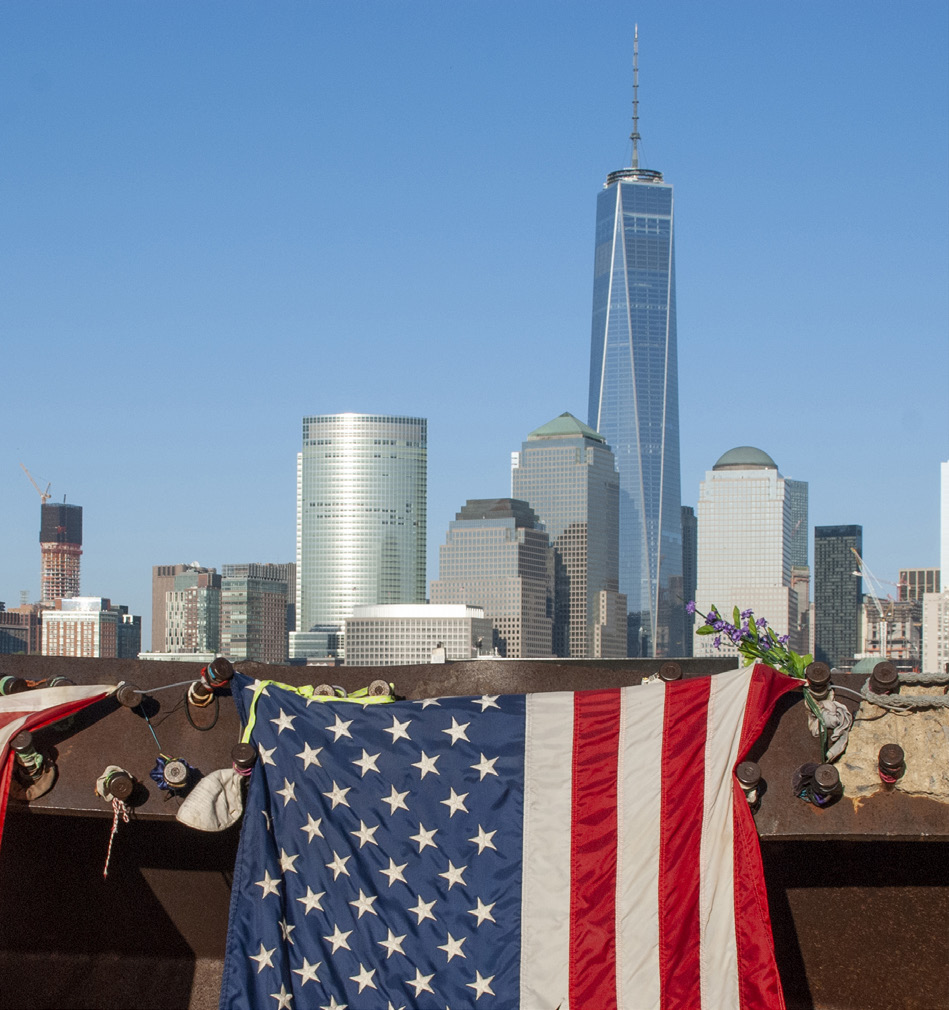 Image shows an American Flag hanging in the foreground of the Lower Manhattan skyline.